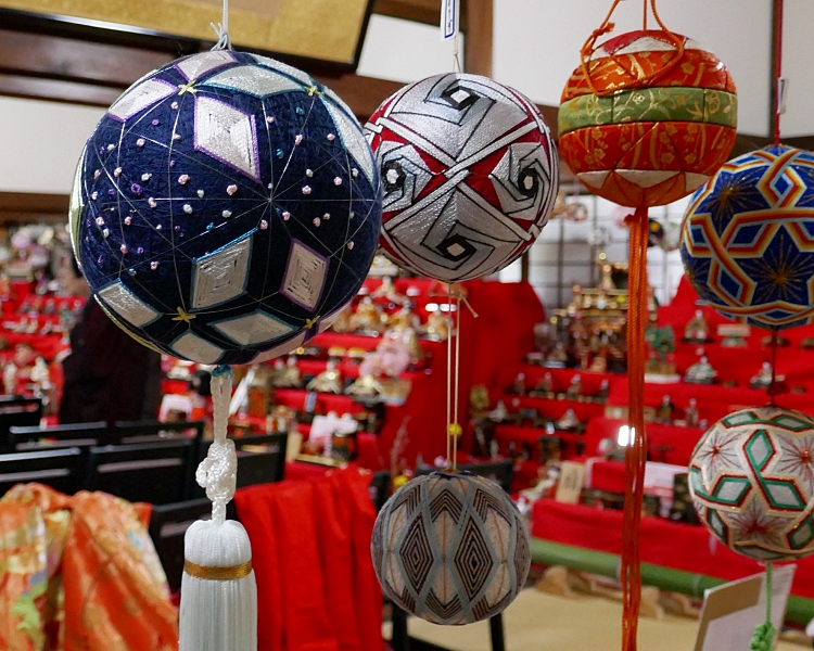 Temari tradizionali con disegni geometrici appese con apparato delle hina sullo sfondo