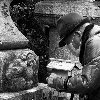 signore cerca di mettere un piccolo sasso nella bocca della lanterna di Hebisu Kitano-Tenmangu